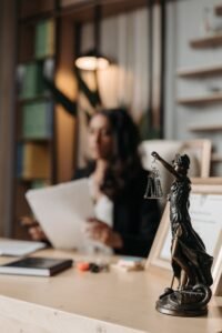 Gros plan d'une figurine de justice sur un bureau avec une avocate floue dans un cadre de bureau.