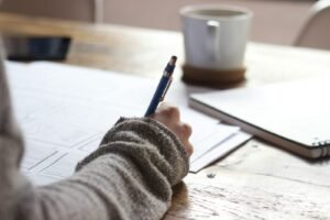 personne écrivant sur une table en bois marron près d'une tasse en céramique blanche