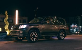 SUV noir stationné sur rue nocturne avec phares allumés