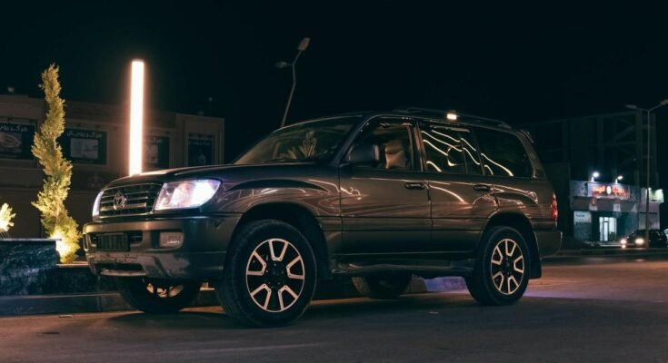 SUV noir stationné sur rue nocturne avec phares allumés