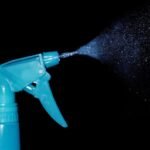 Un pulvérisateur bleu projette une fine brume sur fond noir