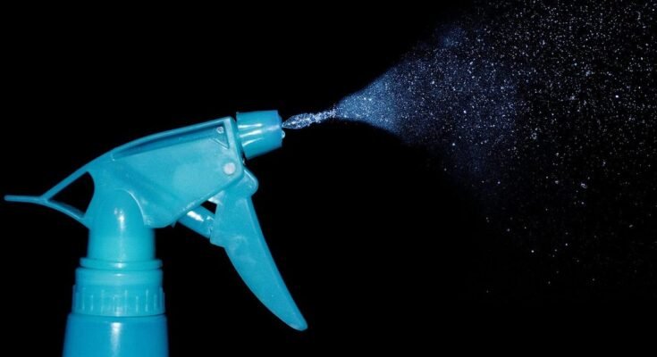 Un pulvérisateur bleu projette une fine brume sur fond noir