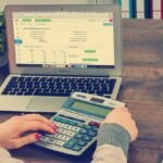 Une main saisit une calculatrice devant un ordinateur portable ouvert