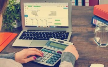 Une main saisit une calculatrice devant un ordinateur portable ouvert