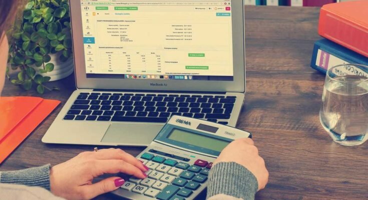 Une main saisit une calculatrice devant un ordinateur portable ouvert