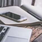 Un smartphone posé sur un cahier ouvert avec stylo et ordinateur portable