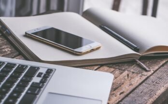 Un smartphone posé sur un cahier ouvert avec stylo et ordinateur portable