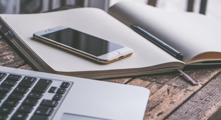 Un smartphone posé sur un cahier ouvert avec stylo et ordinateur portable